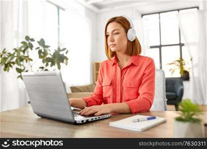 remote job, technology and people concept - young woman in headphones with laptop computer working at home office. woman in headphones with laptop working at home