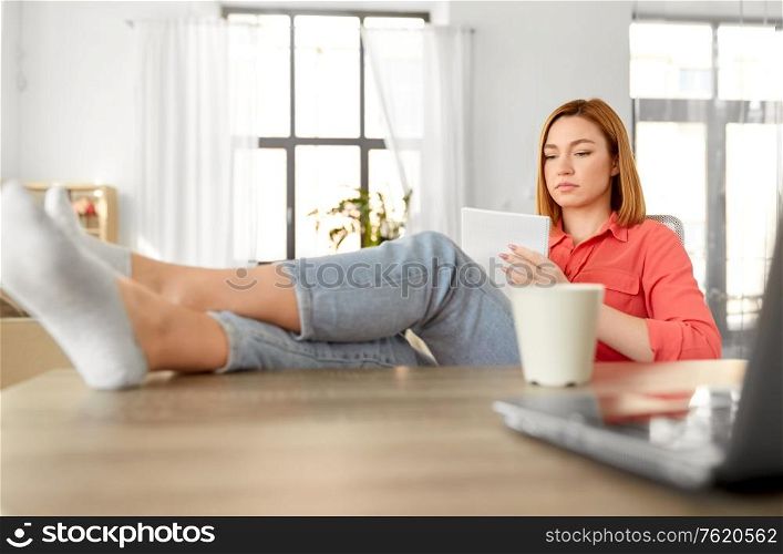 remote job, technology and people concept - young woman with notebook and laptop computer at home office resting feet on table. woman with notebook and laptop at home office