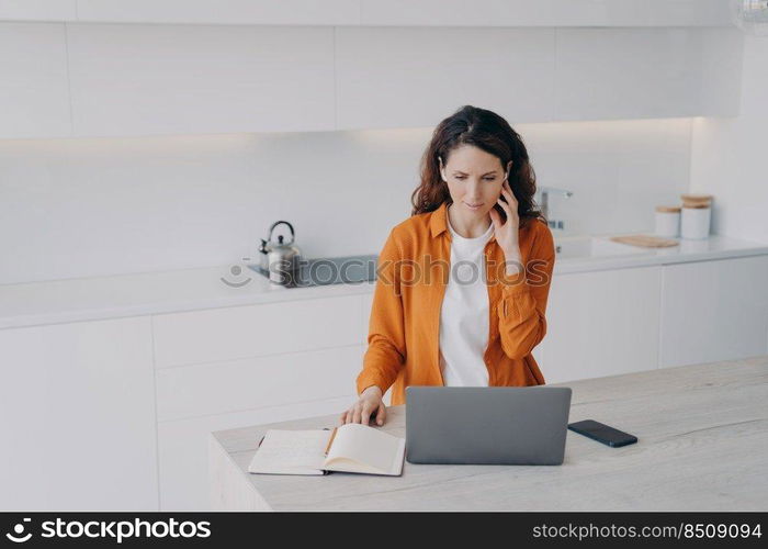 Remote teacher having class via zoom at home. Teacher has conference using earphone and laptop. Happy european woman has conference at kitchen. E-learning and online school on quarantine.. Remote teacher having class via zoom at home. Teacher has conference using earphone and laptop.