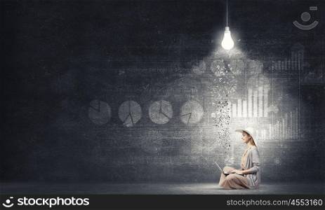 Remote work. Woman in dress and hat sitting on floor and working on laptop
