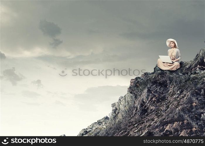 Remote work. Woman in dress and hat sitting on top and working on laptop