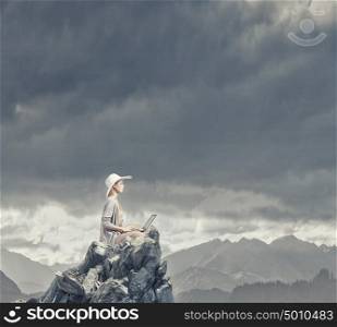 Remote work. Woman in dress and hat sitting on top and working on laptop