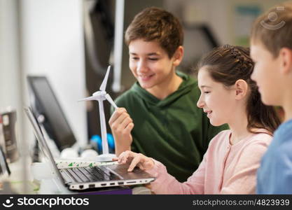 renewable energy, children, technology, science and people concept - group of happy kids or friends with laptop computer and wind turbine model at school