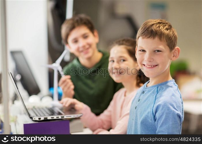 renewable energy, children, technology, science and people concept - group of happy kids or friends with laptop computer and wind turbine model at school