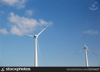 renewable energy, technology and power concept - wind turbines over blue sky. wind turbines over blue sky