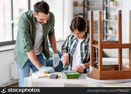 renovation, diy and home improvement concept - father and son in gloves with paint roller painting old wooden table in grey color. father and son painting old table in grey color