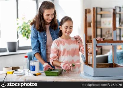 renovation, diy and home improvement concept - happy smiling mother and daughter in gloves with paint roller painting old wooden table in grey color at home. mother and daughter painting old table in grey