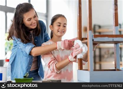 renovation, diy and home improvement concept - happy smiling mother and daughter cleaning old round wooden table surface with tissue. mother and daughter cleaning old table with tissue