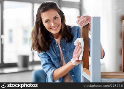 renovation, diy and home improvement concept - happy smiling woman degreasing old wooden table or chair surface with tissue. woman cleaning old table surface with tissue
