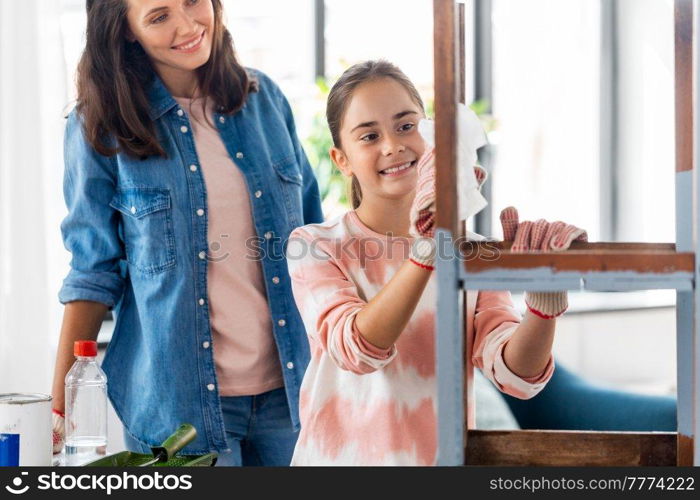 renovation, diy and home improvement concept - mother and daughter applying solvent to tissue and cleaning old wooden table or chair at home. mother and daughter cleaning old wooden table