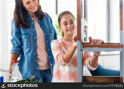 renovation, diy and home improvement concept - mother and daughter applying solvent to tissue and cleaning old wooden table or chair at home. mother and daughter cleaning old wooden table