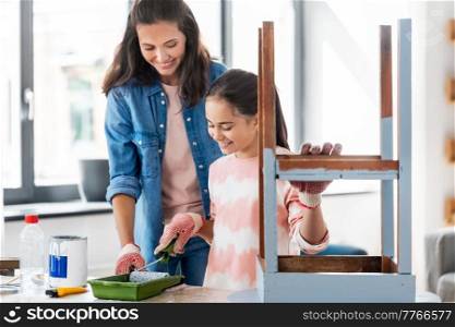 renovation, diy and home improvement concept - mother and daughter in gloves with paint roller painting old wooden table in grey color at home. mother and daughter painting old table at home
