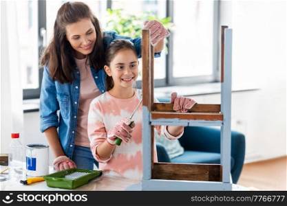renovation, diy and home improvement concept - mother and daughter in gloves with paint roller painting old wooden table in grey color at home. mother and daughter painting old table at home