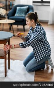 renovation, diy and home improvement concept - woman in gloves with paint brush painting old wooden table to grey color. woman painting old wooden table with grey color