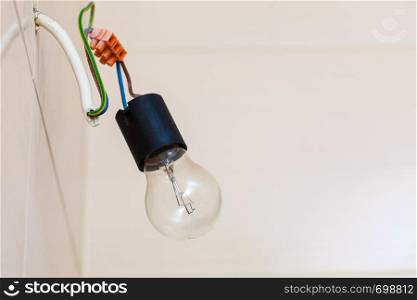 Renovation objects, electricity details concept. Small bulb hanging on bare wires, white tiles in background.. Small bulb hanging on wires