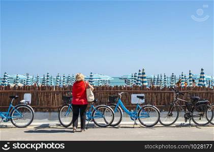 Rental bikes on the beach. Blue bicycles on the street. Many beach umbrellas.