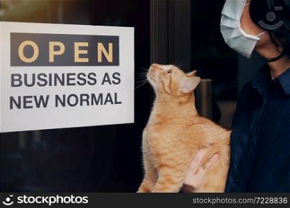 Reopening for business adapt to new normal in the novel Coronavirus COVID-19 pandemic. A cat with their owner person wearing mask in front of business shop with open sign OPEN BUSINESS AS NEW NORMAL