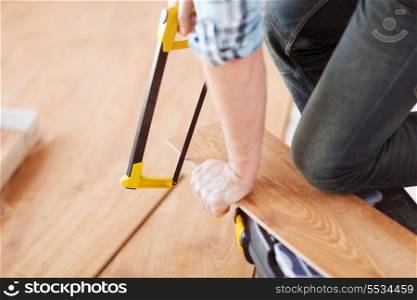 repair, building and home concept - close up of male hands cutting parquet floor board with saw