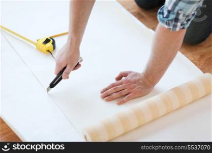 repair, building and home concept - close up of male hands cutting wallpaper