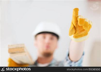 repair, building and home concept - close up of male in gloves and helmet carrying wooden boards on shoulder and pointing finger