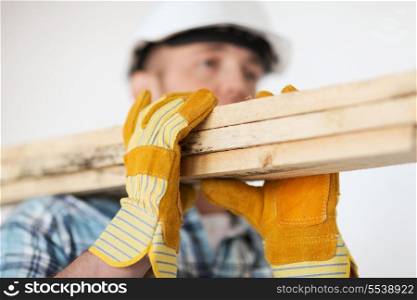 repair, building and home concept - close up of male in gloves and helmet carrying wooden boards on shoulder