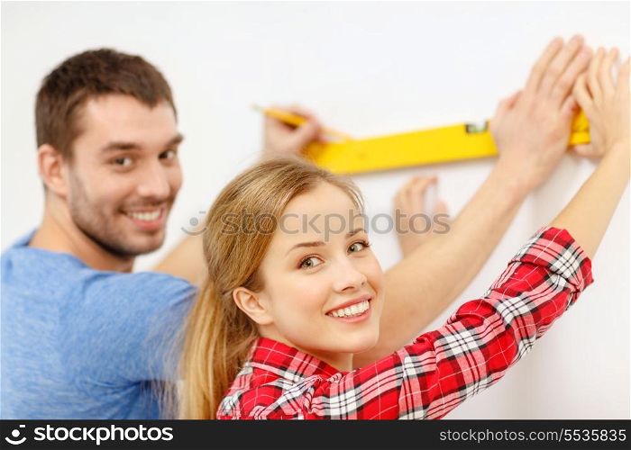 repair, building and home concept - smiling couple building new home using spirit level to measure