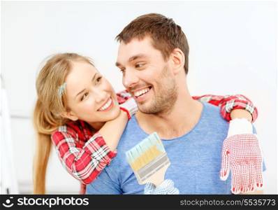 repair, building and home concept - smiling couple covered with paint with paint brush