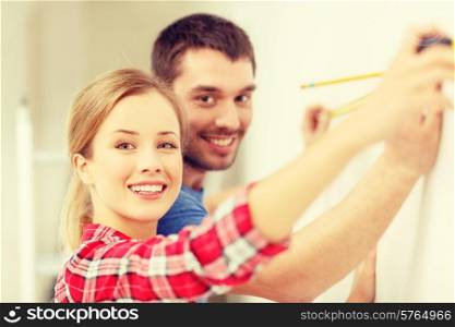 repair, building and home concept - smiling couple measuring wall