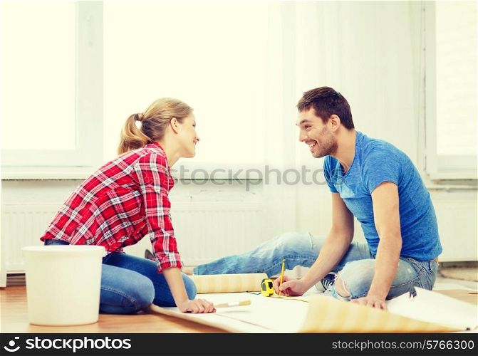 repair, building and home concept - smiling couple measuring wallpaper