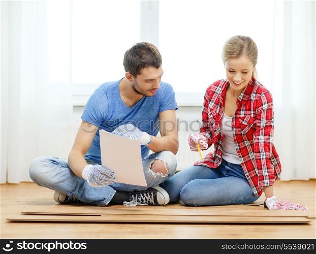 repair, building and home concept - smiling couple measuring wood flooring