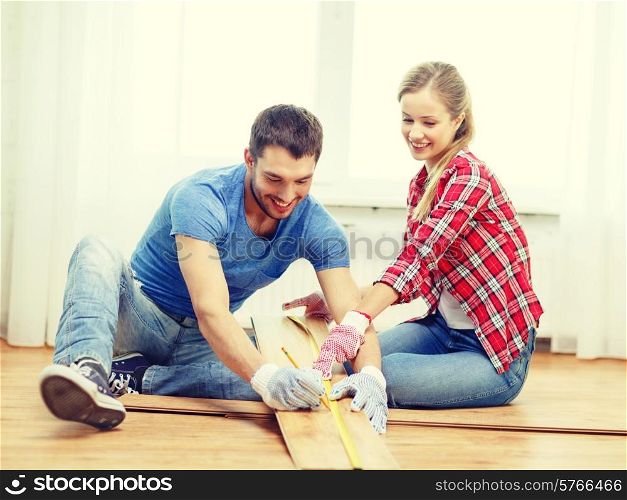 repair, building and home concept - smiling couple measuring wood flooring