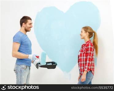 repair, building and home concept - smiling couple painting big heart on wall at home