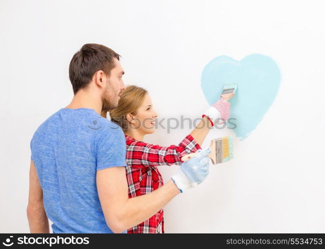 repair, building and home concept - smiling couple painting small heart on wall at home