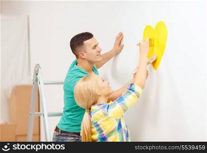 repair, building and home concept - smiling couple painting small heart on wall at home
