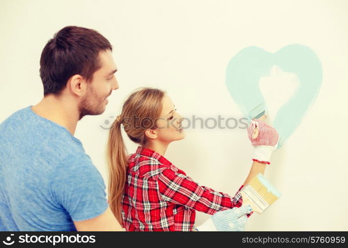 repair, building and home concept - smiling couple painting small heart on wall at home