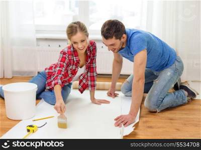 repair, building and home concept - smiling couple smearing wallpaper with glue
