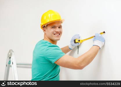 repair, building and home concept - smiling man in yellow protective helmet measuring wall