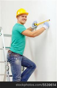 repair, building and home concept - smiling man in yellow protective helmet measuring wall