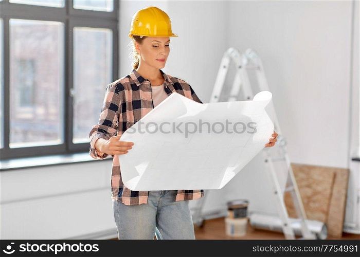 repair, building and real estate concept - woman in helmet with blueprint sitting on floor at home. woman in helmet with blueprint at home