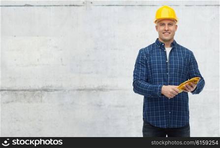repair, building, construction, people and maintenance concept - smiling man in helmet with gloves over gray concrete wall background