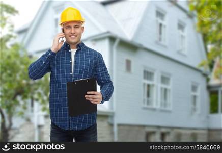 repair, building, construction, real estate and maintenance concept - smiling man or builder in helmet with clipboard calling on smartphone over living house background