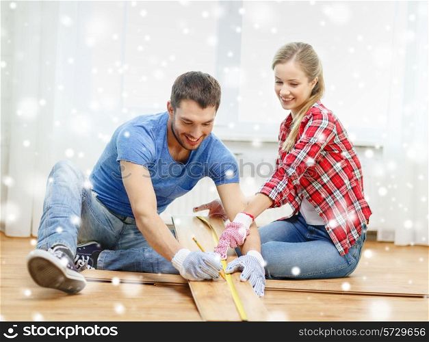 repair, building, family, people and home concept - smiling couple measuring parquet plank on floor