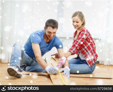 repair, building, family, people and home concept - smiling couple measuring parquet plank on floor