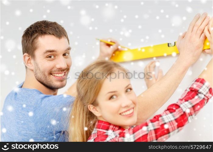 repair, building, people and new home concept - smiling couple measuring wall by spirit level