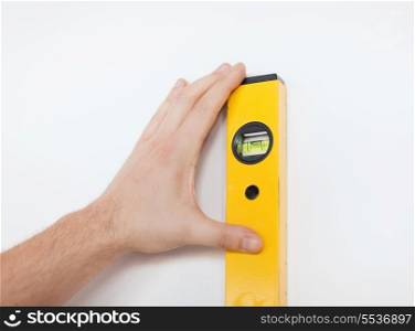 repair, building, technology and home concept - close up of male with spirit level mesuring wall