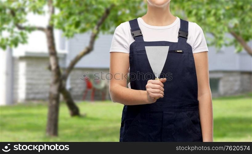 repair, construction and building concept - close up of female plasterer or builder with putty knife over living house yard with garden background. close up of female builder with putty knife