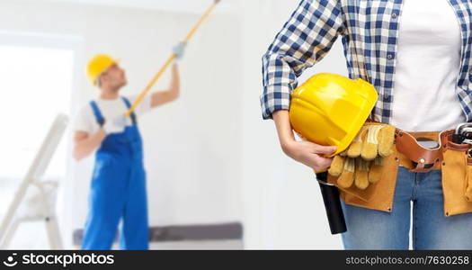 repair, construction and building concept - close up of woman or builder with helmet and working tools on belt over painting works on background. woman or builder with helmet and working tools