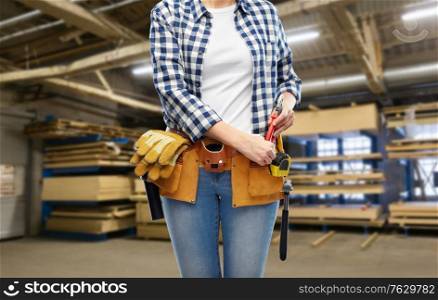 repair, construction and building concept - female worker with pliers and working tools on belt over workshop at woodworking factory background. female worker with tools on belt at factory