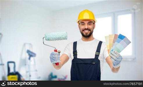 repair, construction and building concept - happy smiling male worker or builder in yellow helmet and overall with paint roller and color palettes over room with equipment on background. male builder with paint roller and color palettes