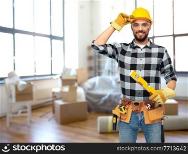 repair, construction and building concept - happy smiling male worker or builder in helmet with level over home room background. happy male builder in helmet with level at home